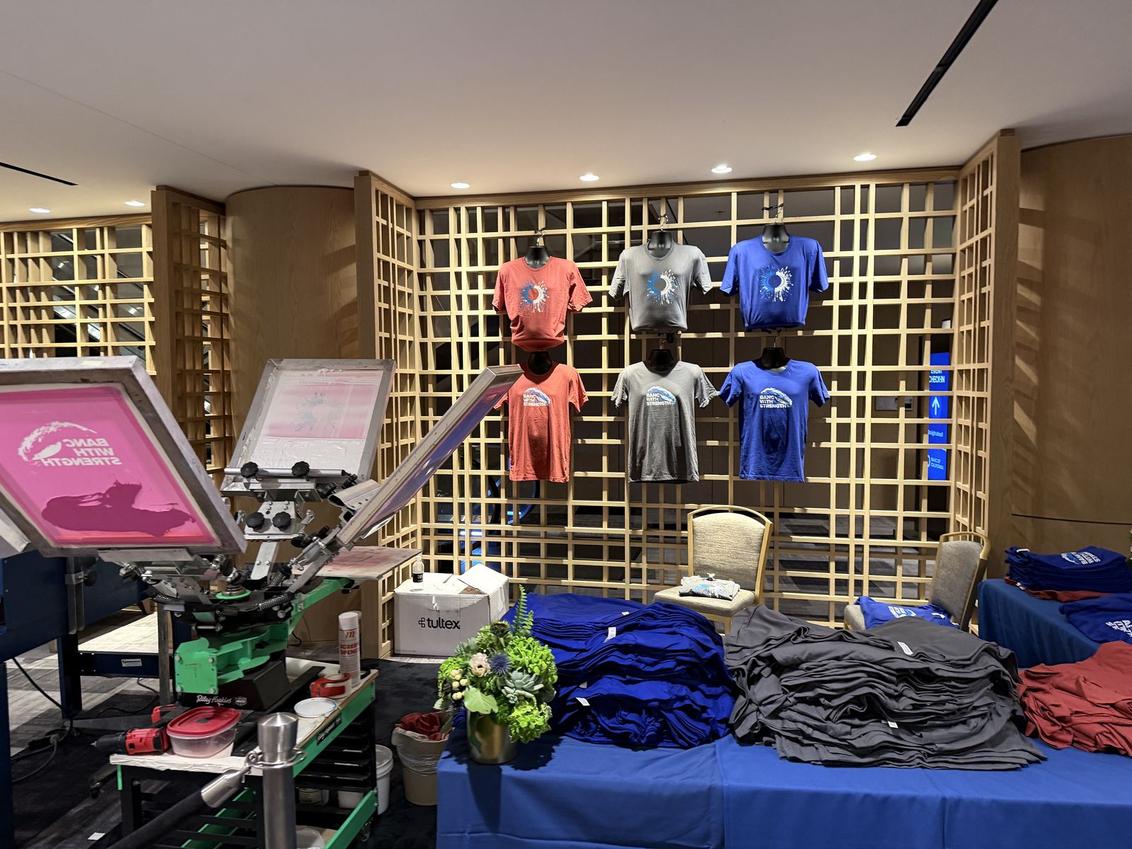 Apparel display wall with garments and flowers staged beside personalization equipment in a hotel lounge